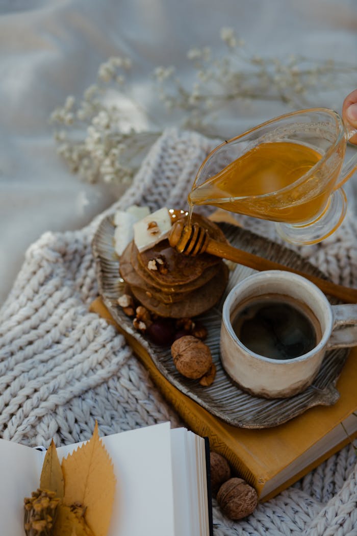 Rustic still life of pancakes, honey, and coffee on a cozy knit blanket.